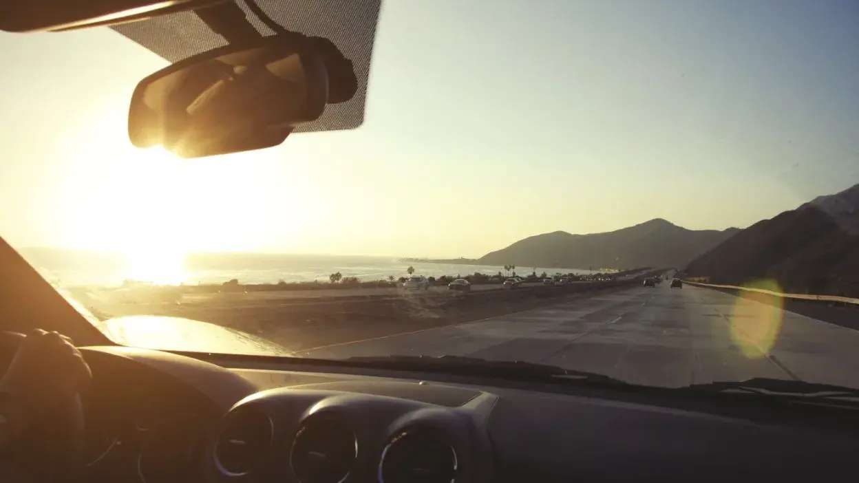 Vista da estrada a partir do interior de um carro com o sol baixo e intenso à frente dificultando a visibilidade.