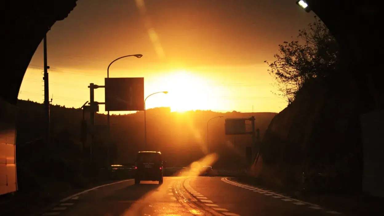Estrada com carros a conduzir em direção ao sol poente, visibilidade reduzida pela luz intensa.