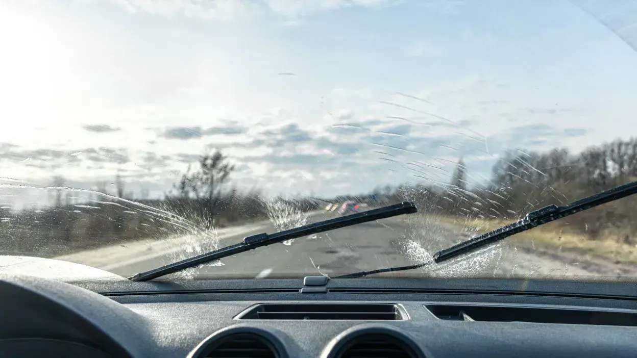 Vista interior de um carro com limpa vidros a limpar o para-brisas sujo durante a condução numa estrada.