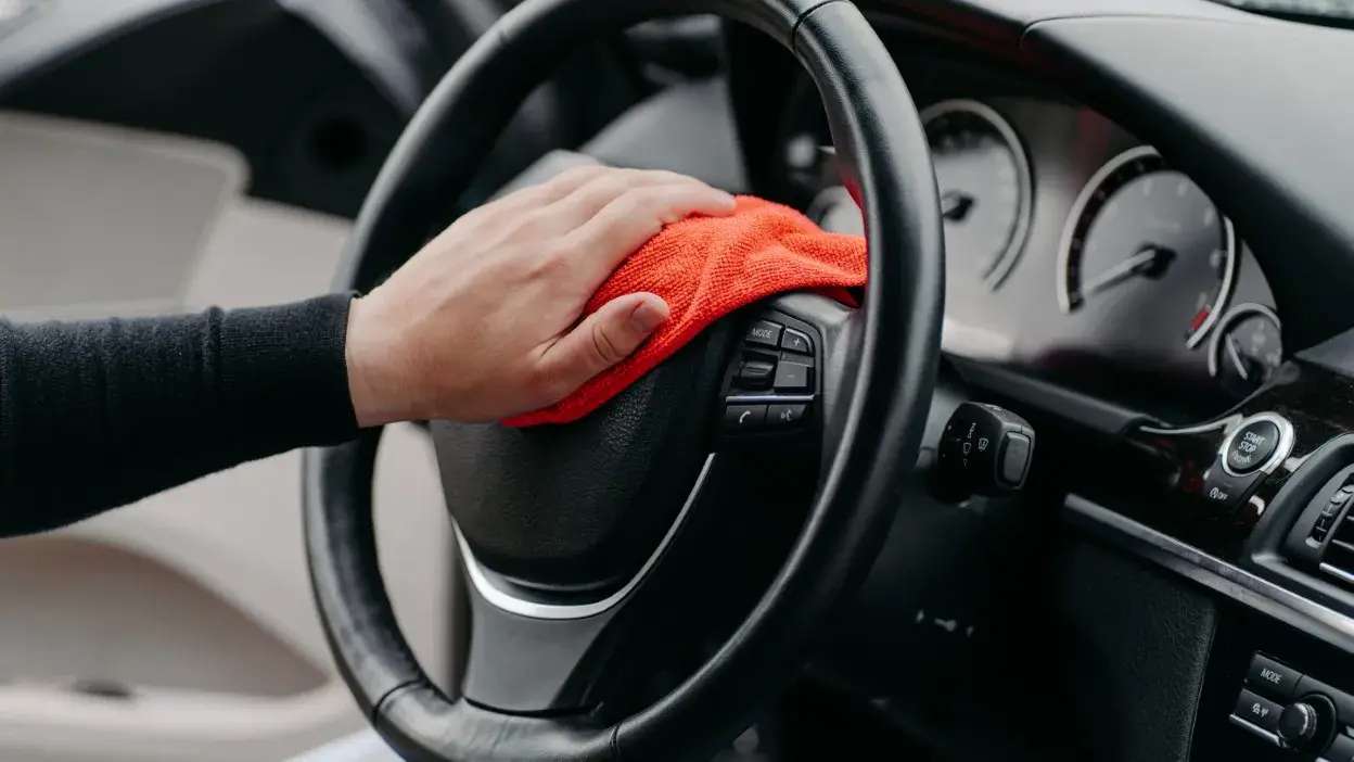 Mão a limpar volante de carro com pano vermelho microfiber