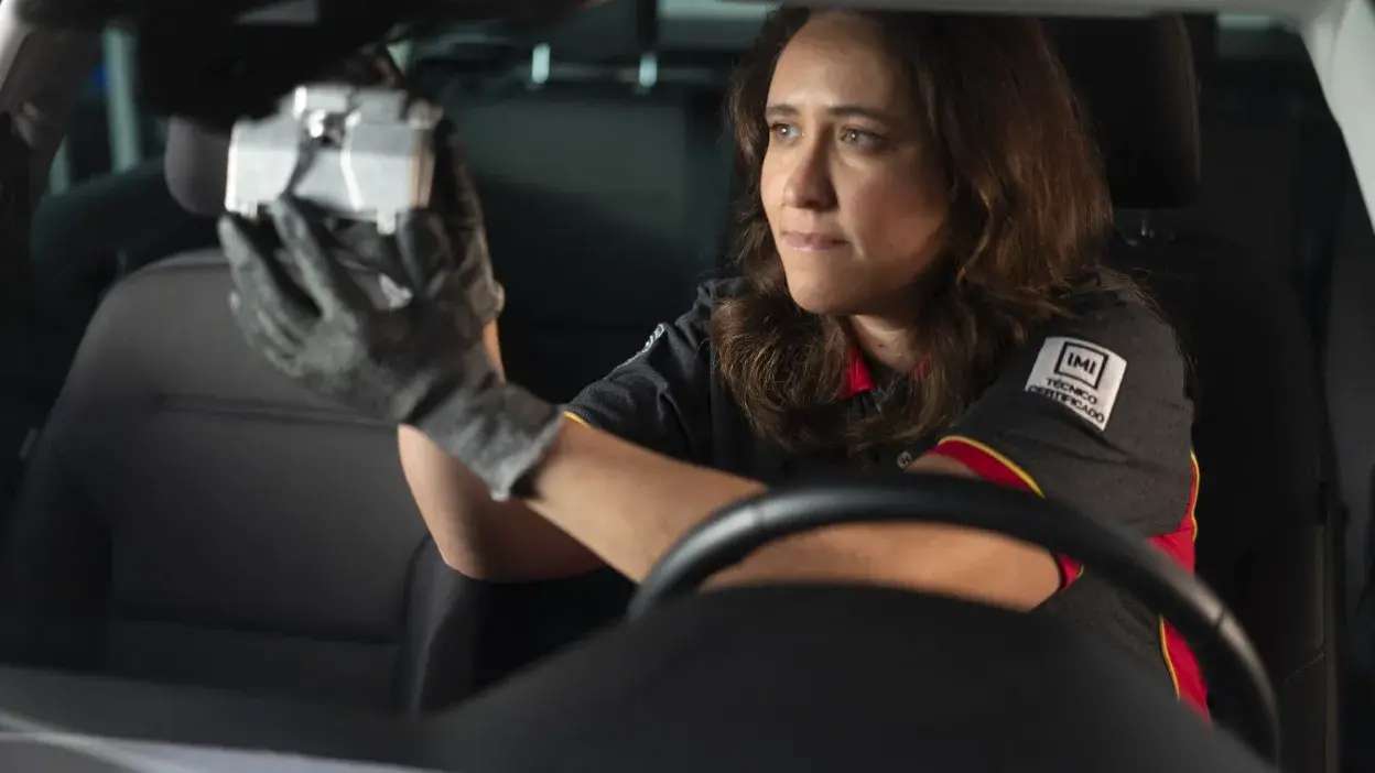 Mulher com uniforme a calibrar sensor dentro de um carro, usando luvas pretas.