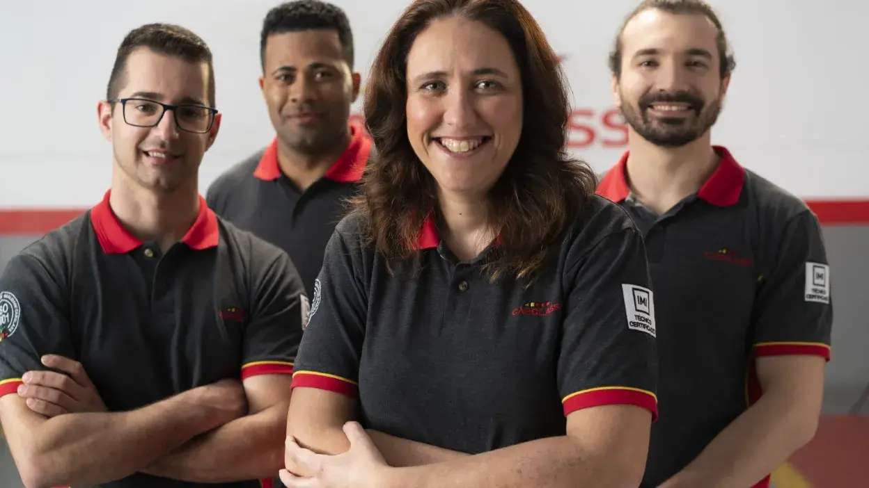 Quatro técnicos da Carglass com uniformes pretos e golas vermelhas, sorridentes e em pose de grupo.