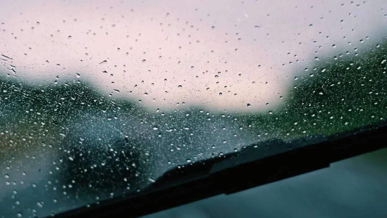 Gotas de chuva num para-brisas de carro com limpa-vidros em movimento.