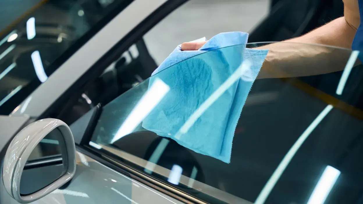 Mão a limpar vidro lateral de carro com pano azul