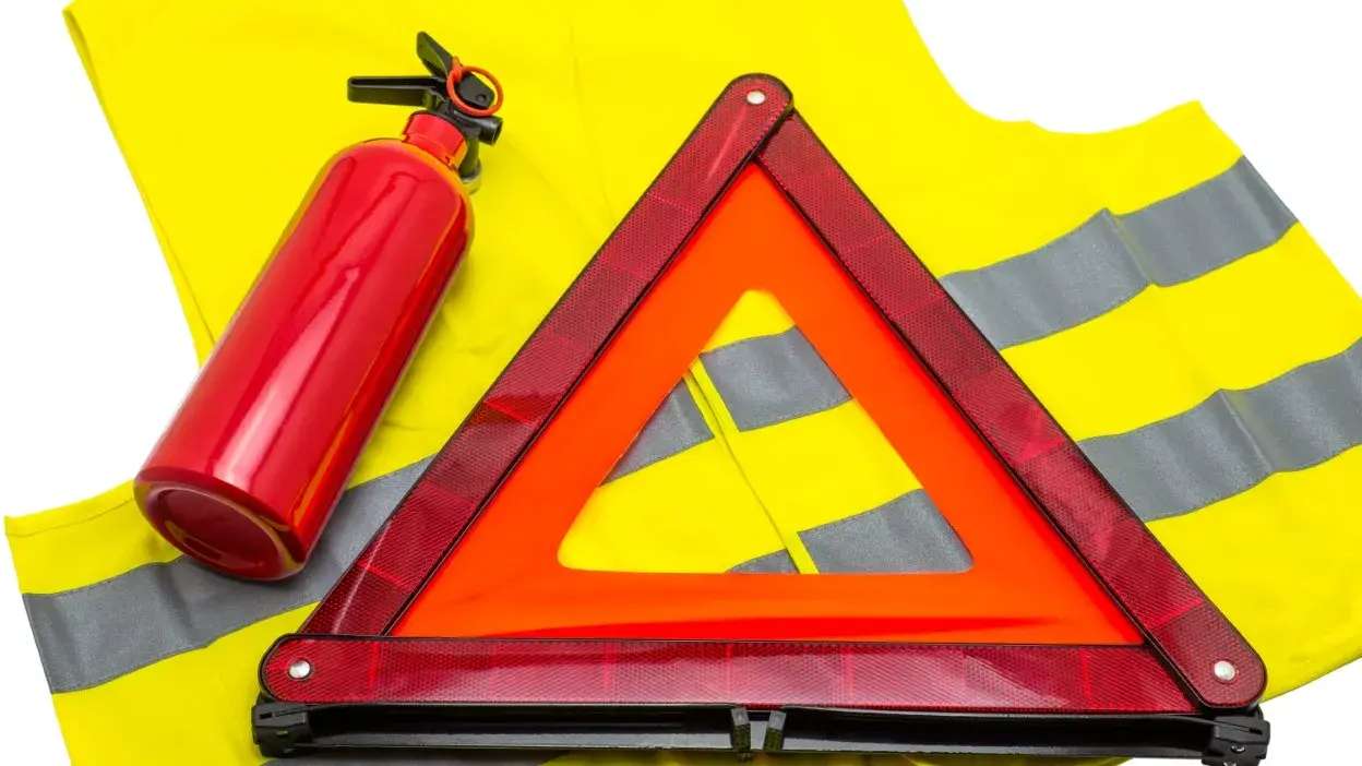 Extintor, colete refletor e triângulo de sinalização sobre fundo branco
