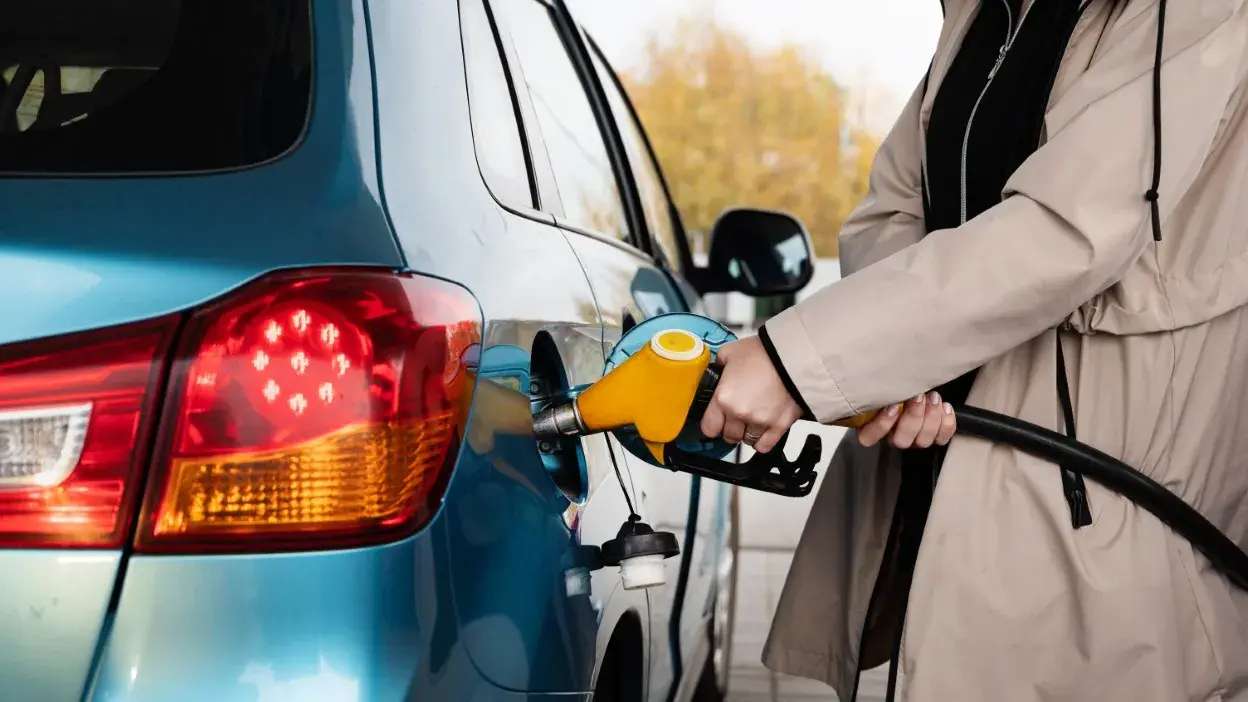 Pessoa a abastecer um carro azul com gasolina numa bomba amarela.