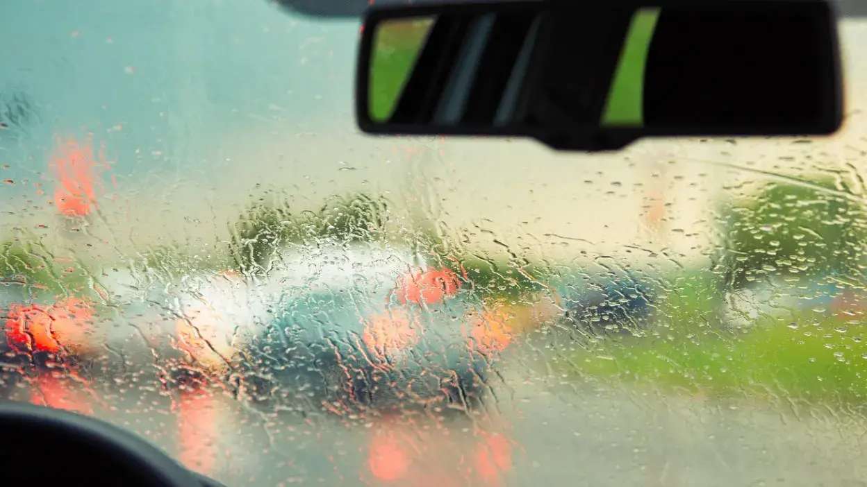 Vista desfocada de carros na estrada através de vidro com gotas de chuva.