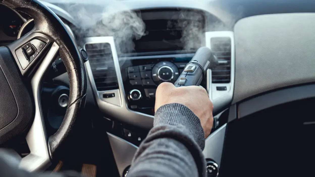 Pessoa a limpar o sistema de ar condicionado de um carro com equipamento de vapor.