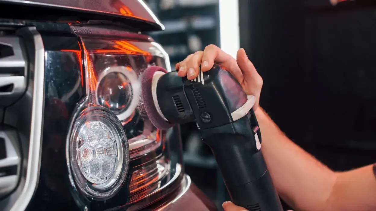 Pessoa a polir o farol de um carro com uma máquina polidora elétrica
