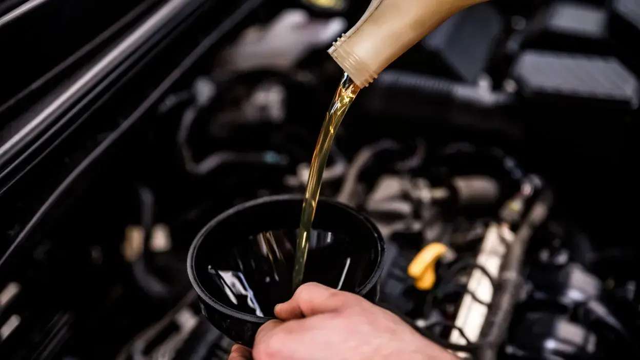 Pessoa a verter óleo novo para o motor do carro usando um funil preto.