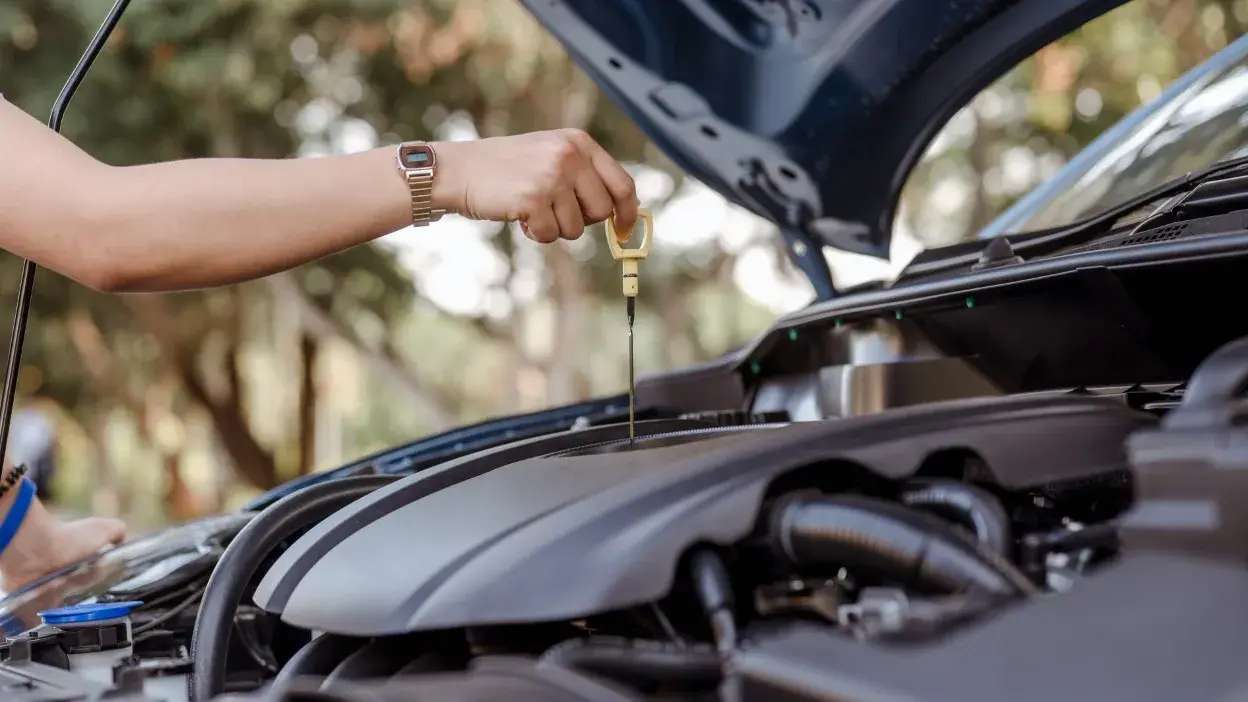 Pessoa a retirar vareta para verificar óleo do motor de um carro com capot aberto