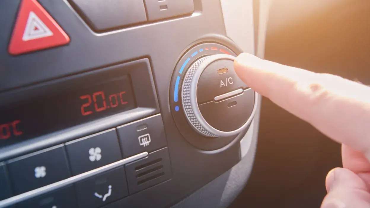 Mão a ajustar o termóstato do ar condicionado num carro, com temperatura a 20ºC.