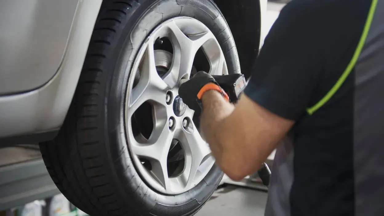 Mecânico a apertar parafuso da roda de um carro com ferramenta elétrica