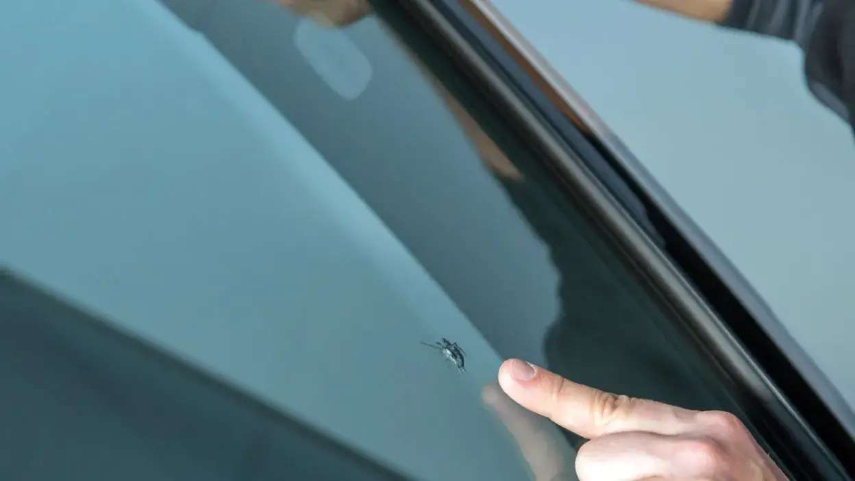 Mão a apontar para vidro de carro com fissura pequena.