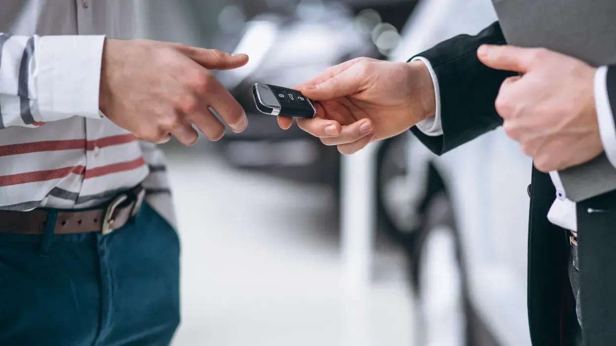 Mãos de duas pessoas a trocar uma chave de carro num ambiente de concessionário automóvel.