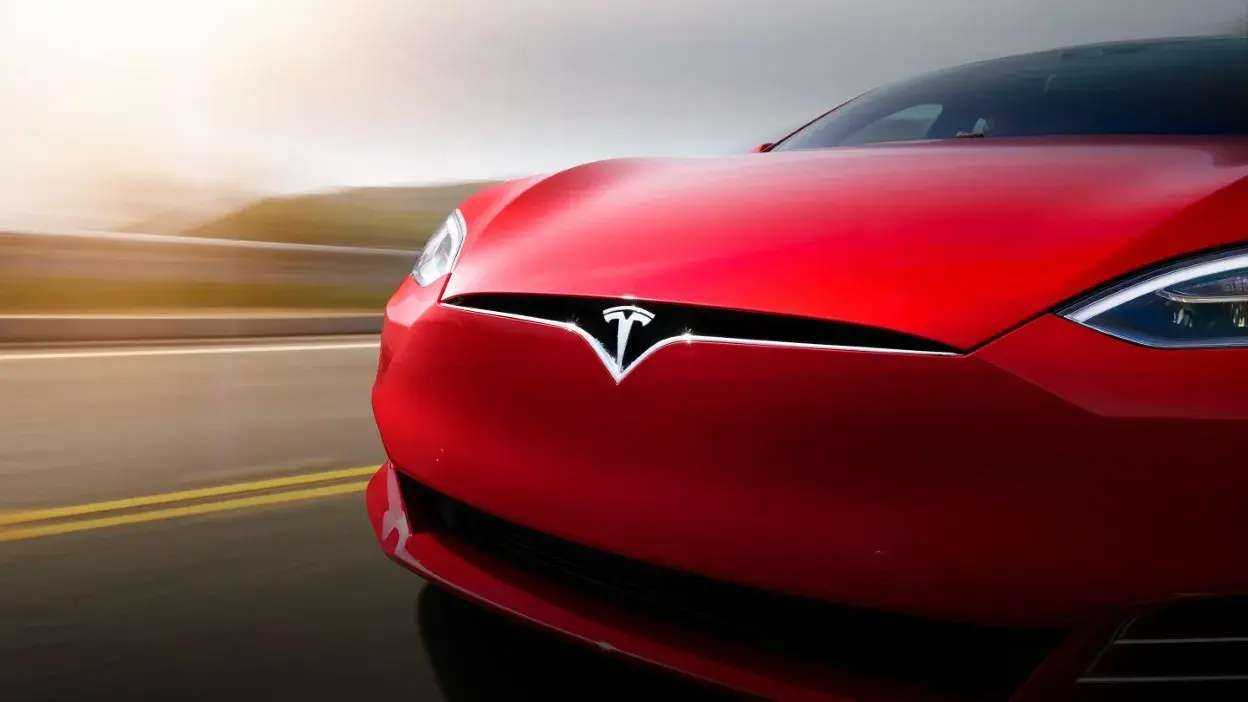 Vista frontal de um carro Tesla vermelho em movimento numa estrada.