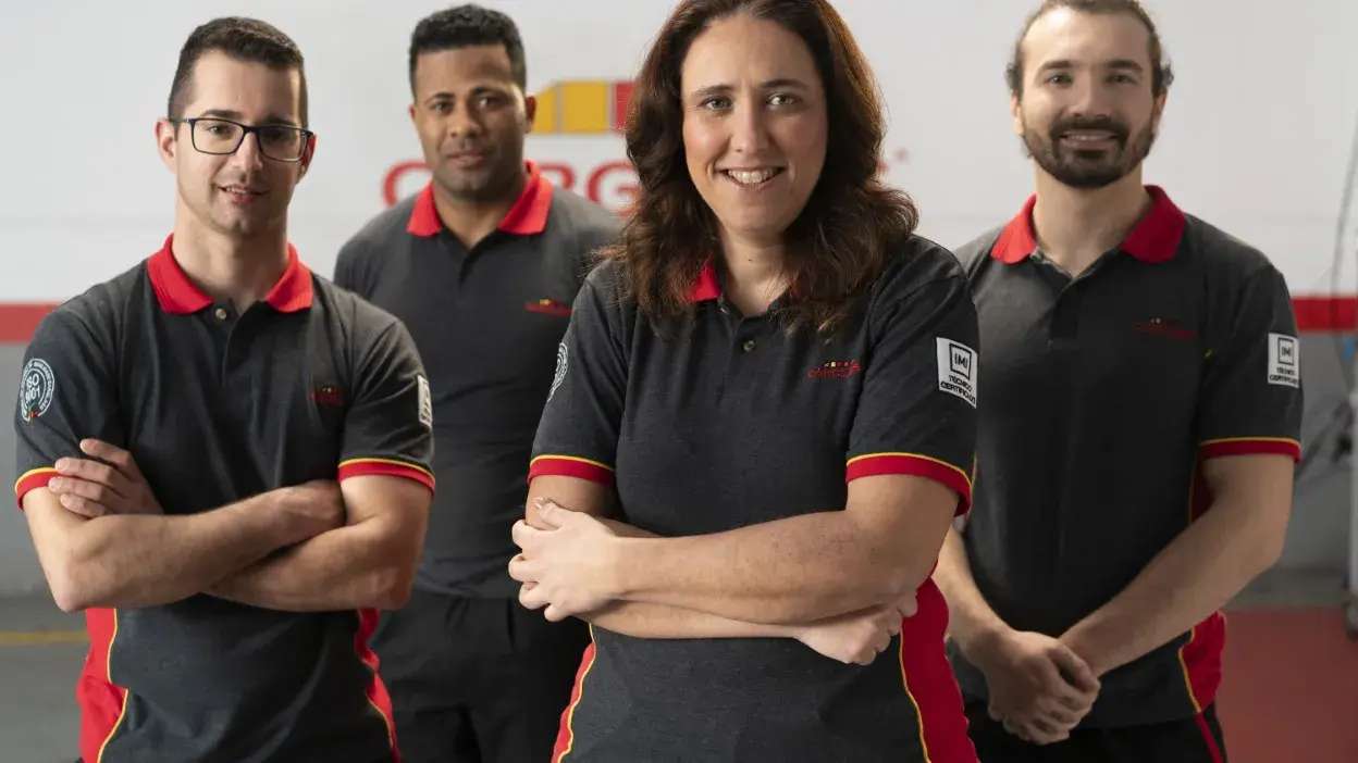 Quatro pessoas com uniformes pretos com detalhes vermelhos, posando com os braços cruzados num ambiente de trabalho.