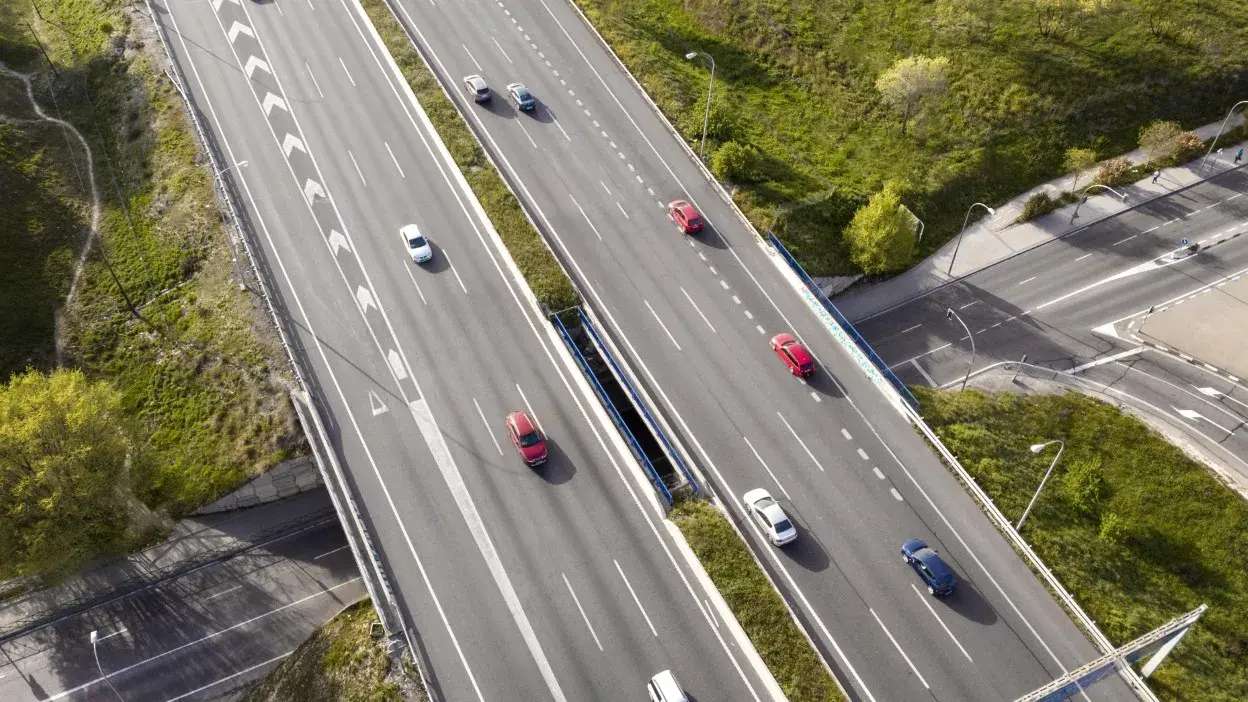 Vista aérea de uma autoestrada com vários carros em movimento e áreas verdes ao redor.