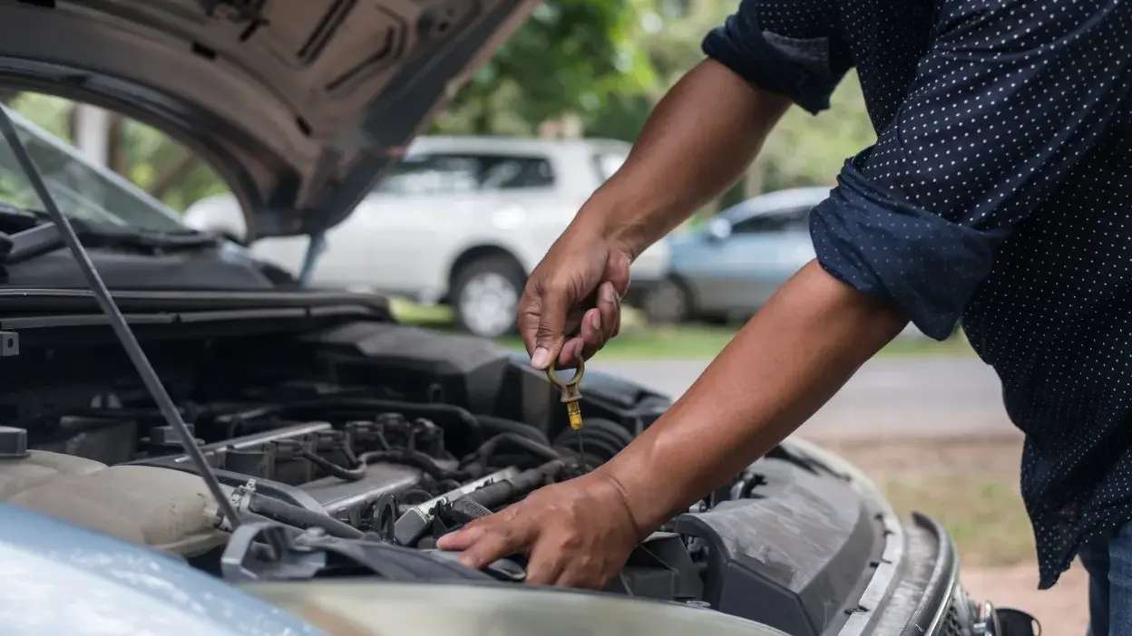 Pessoa a verificar o nível de óleo no motor de um carro com capot aberto.