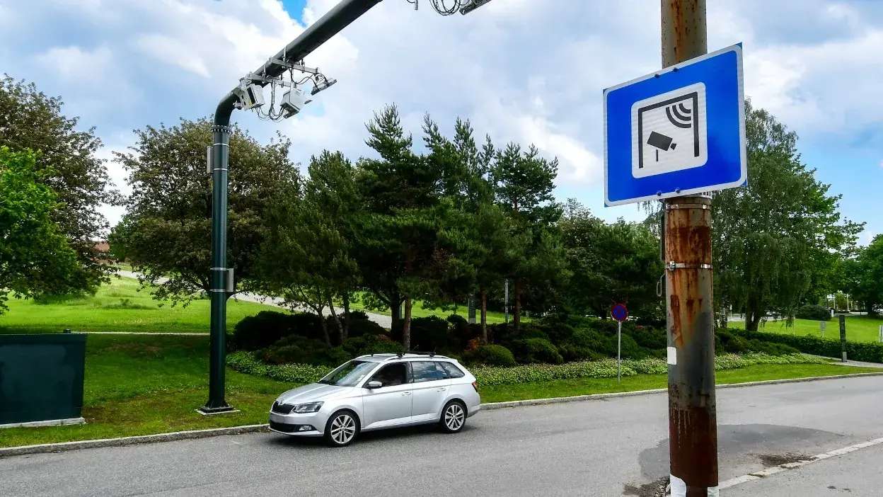 Carro a passar por sistema de câmaras para pagamento automático de portagens numa estrada com sinalização visível.