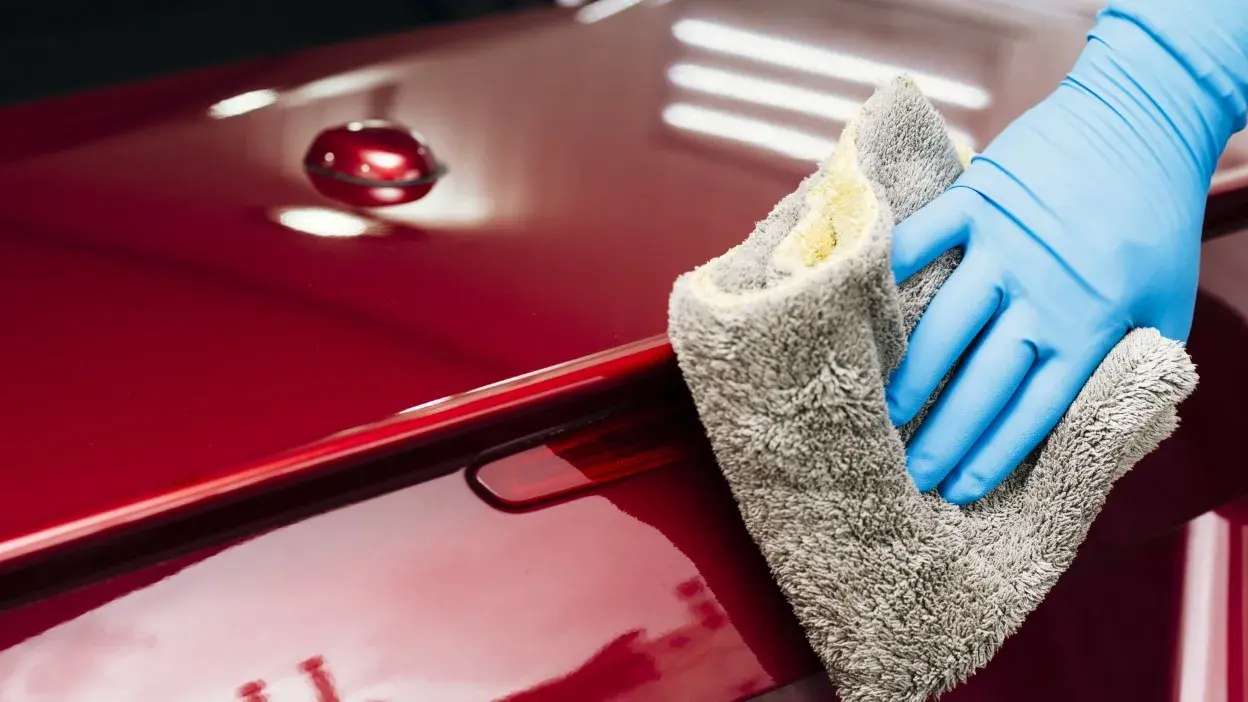 Mão com luva azul a polir carro vermelho com pano cinzento de microfibra