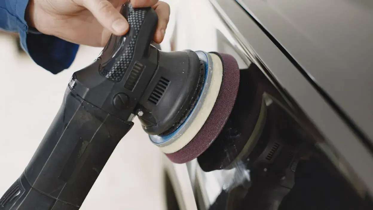 Pessoa a polir a superfície de um carro com uma máquina polidora elétrica preta.