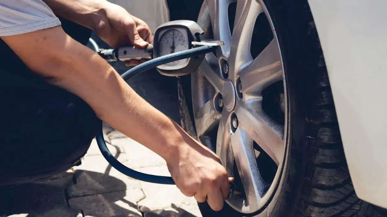 Pessoa a medir a pressão do pneu de um carro com manómetro portátil