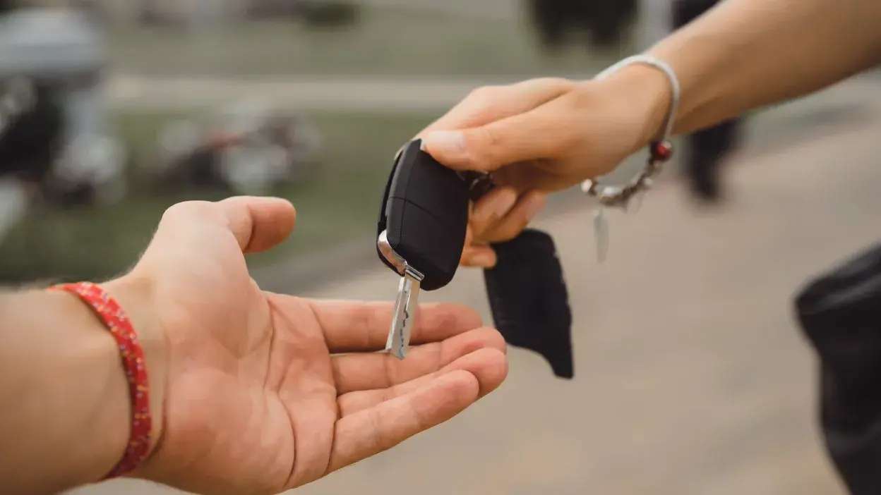 Mão a entregar chave de carro a outra mão num ambiente exterior