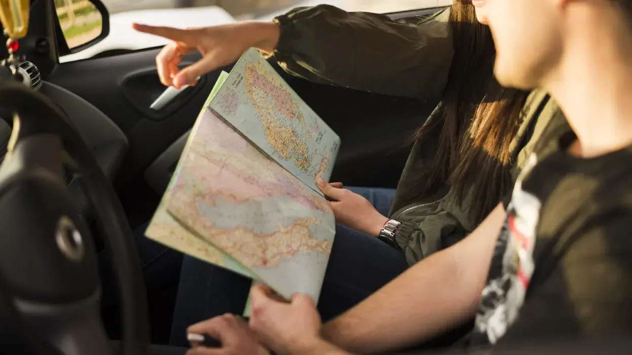Duas pessoas no interior de um carro a consultar um mapa para planear uma viagem de carro.