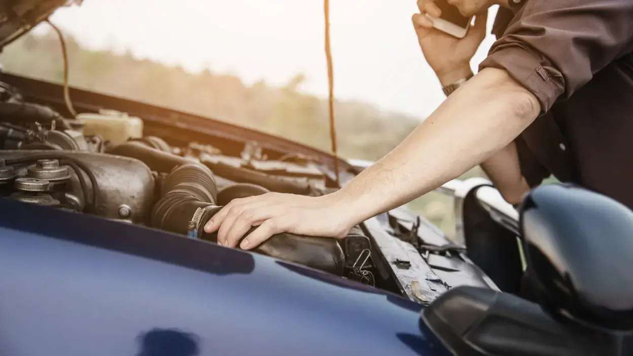 Pessoa a verificar o motor de um carro com o capot aberto e a falar ao telemóvel.