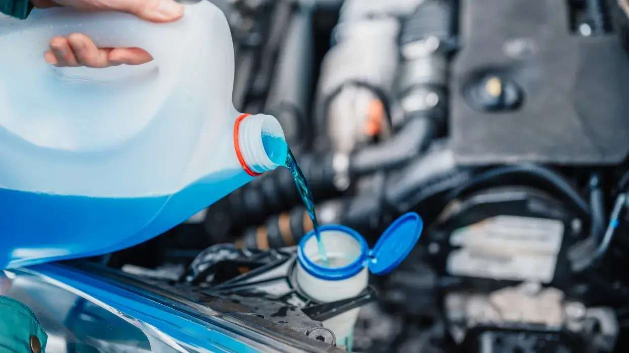 Pessoa a verter líquido azul no depósito do carro com motor ao fundo