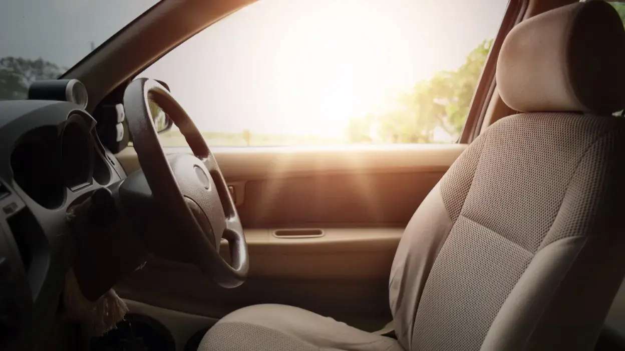 Interior de carro com volante e banco dianteiro iluminados pela luz solar através da janela lateral.