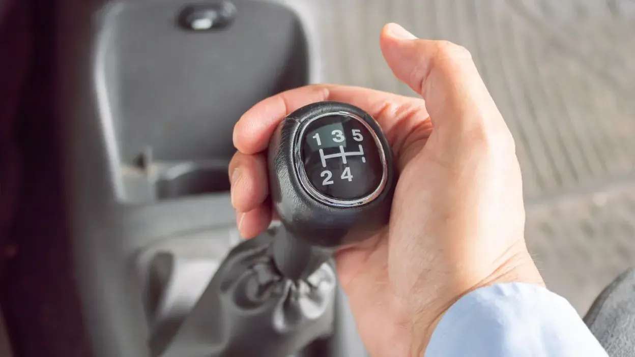 Mão a segurar a alavanca de mudanças de um carro com caixa manual, mostrando as posições das velocidades.