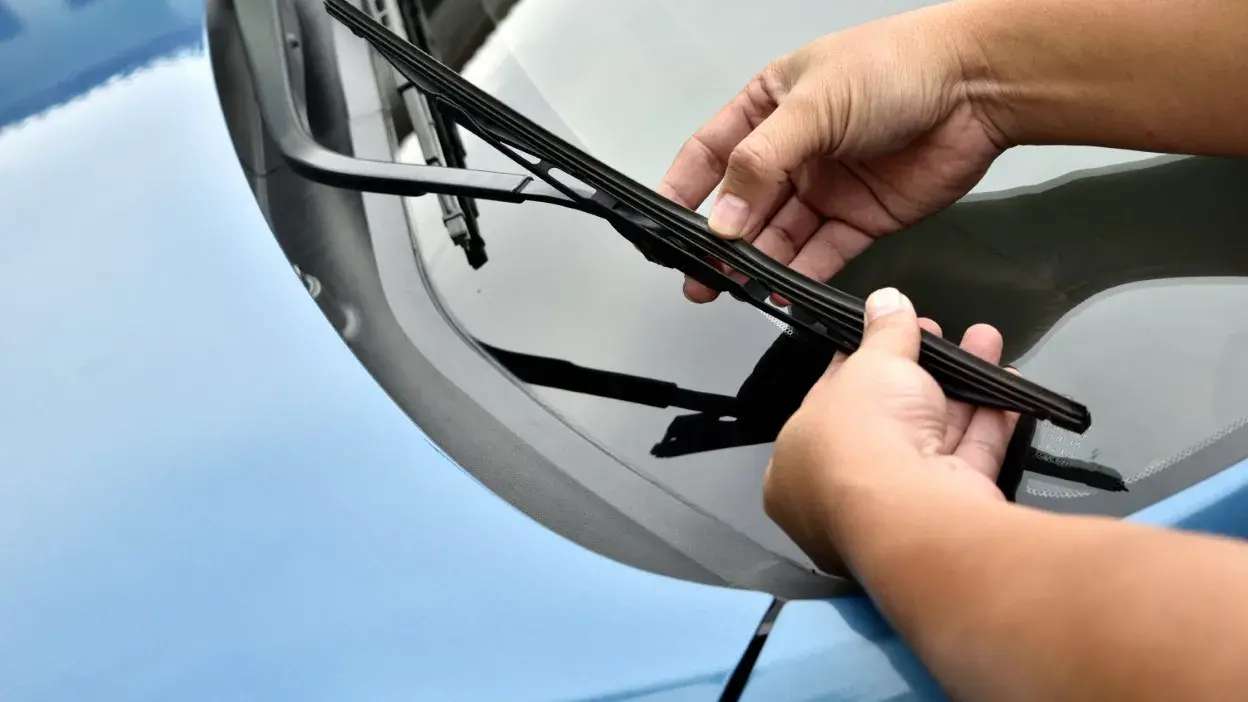 Mãos a trocar a palheta do limpa para-brisas de um carro azul