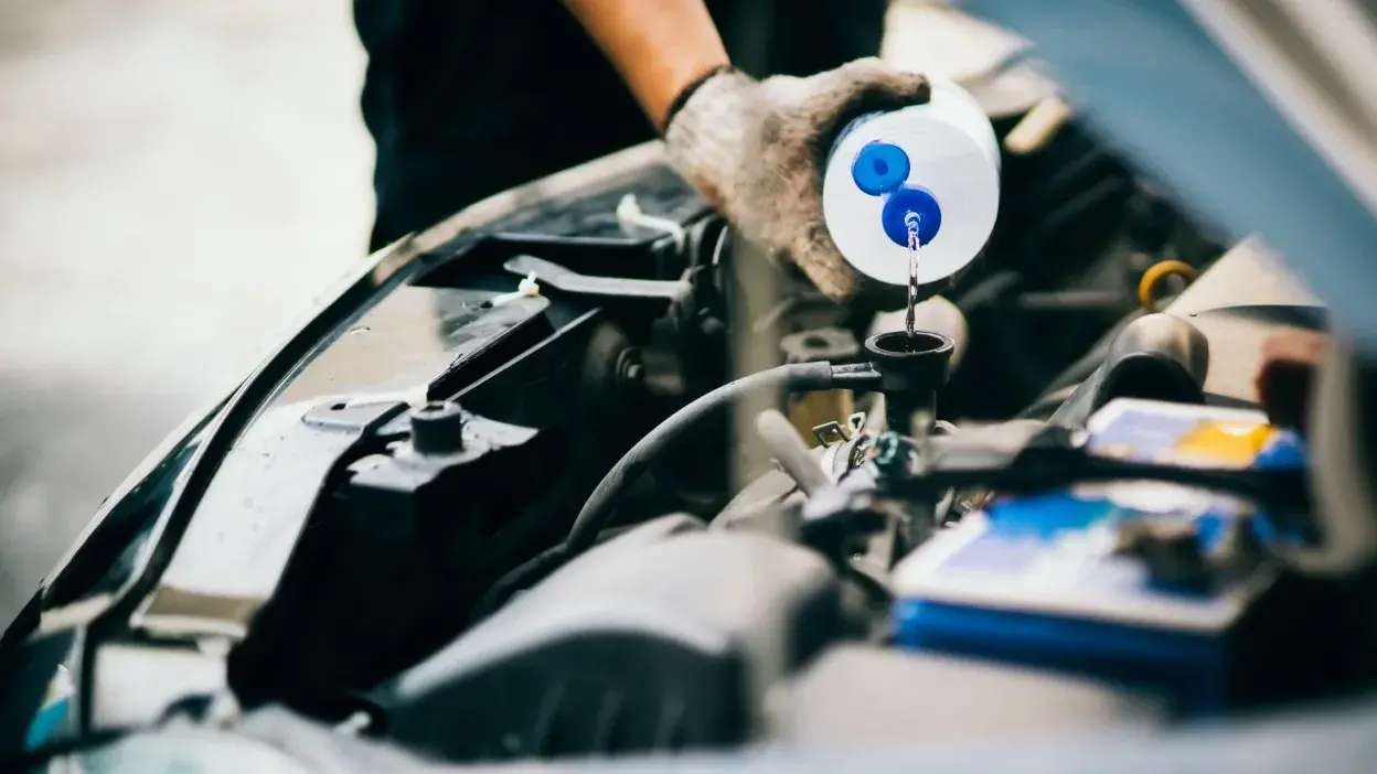 Pessoa a verter líquido no radiador de um carro com luva de proteção