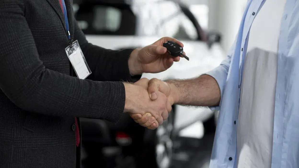 Duas pessoas a apertar as mãos, uma delas entrega uma chave de carro preta.