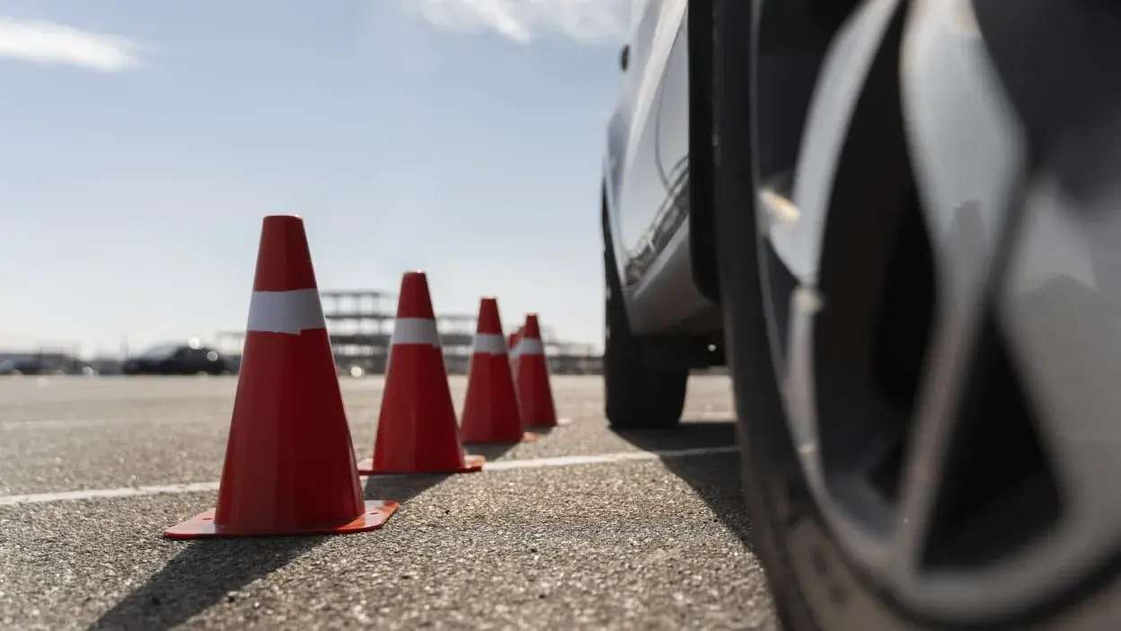 Carro a passar entre cones de trânsito num parque de estacionamento durante aula de condução.