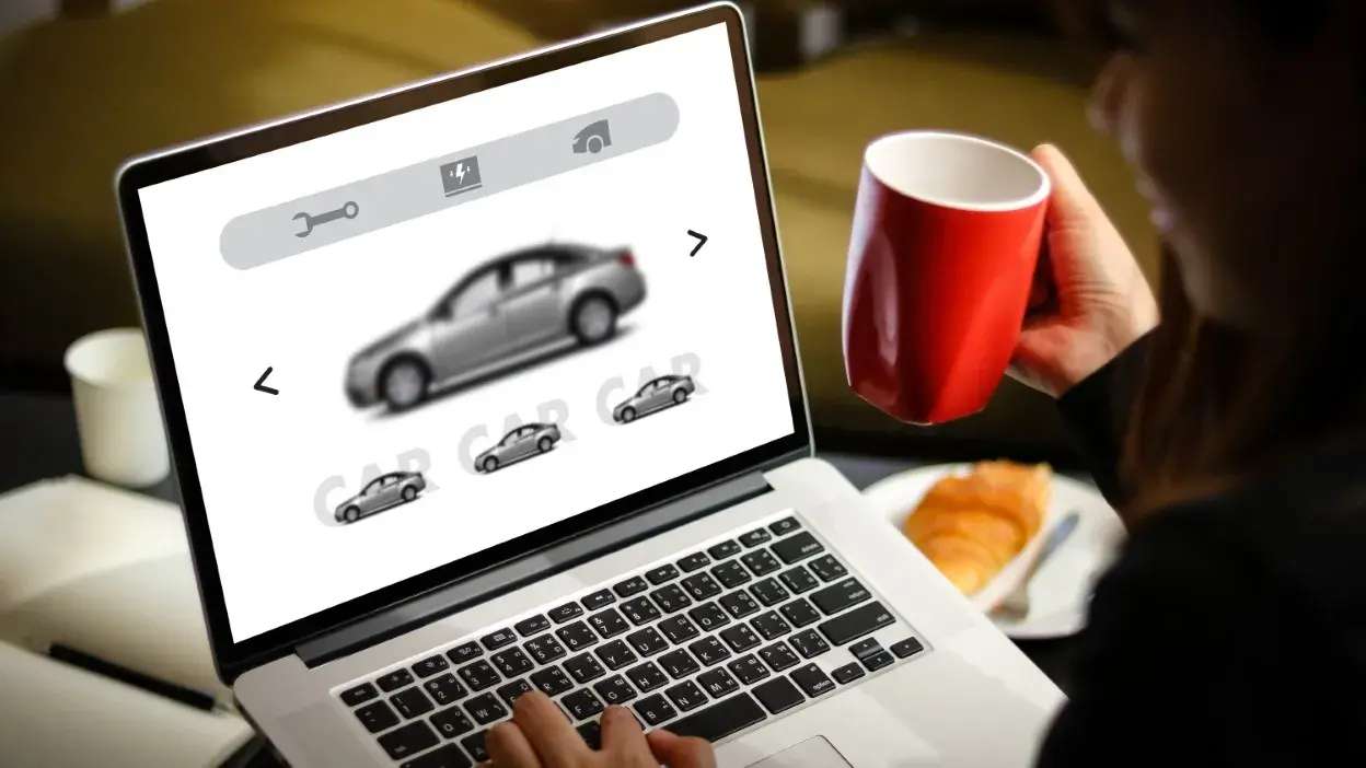 Pessoa a escolher um carro num site num portátil enquanto segura uma chávena vermelha.