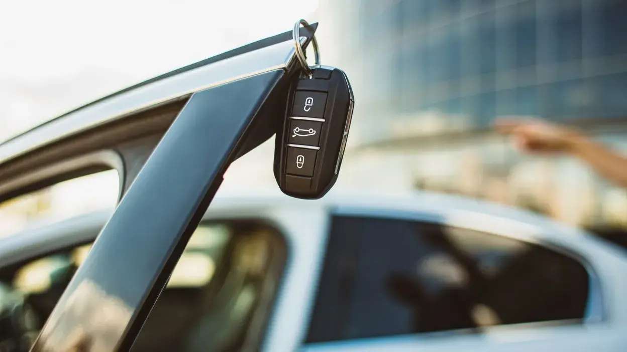 Chave de carro pendurada na porta aberta de um veículo branco estacionado.