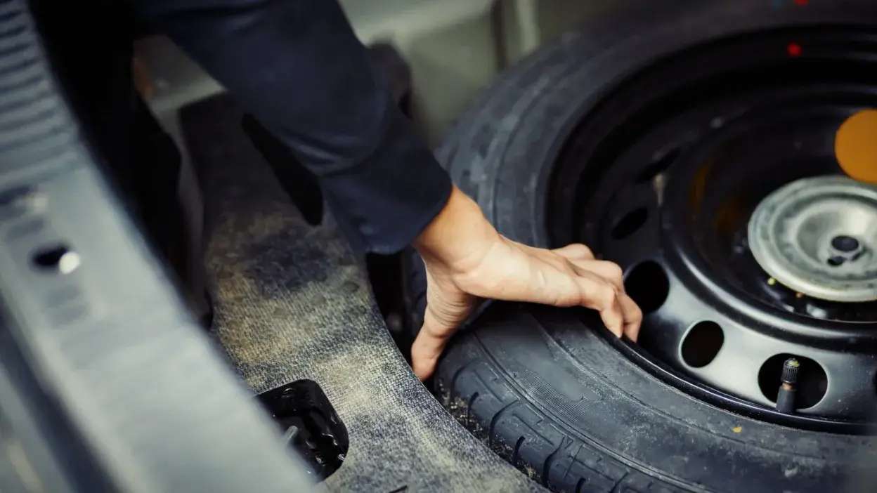 Mão a retirar pneu suplente do porta-malas de um carro