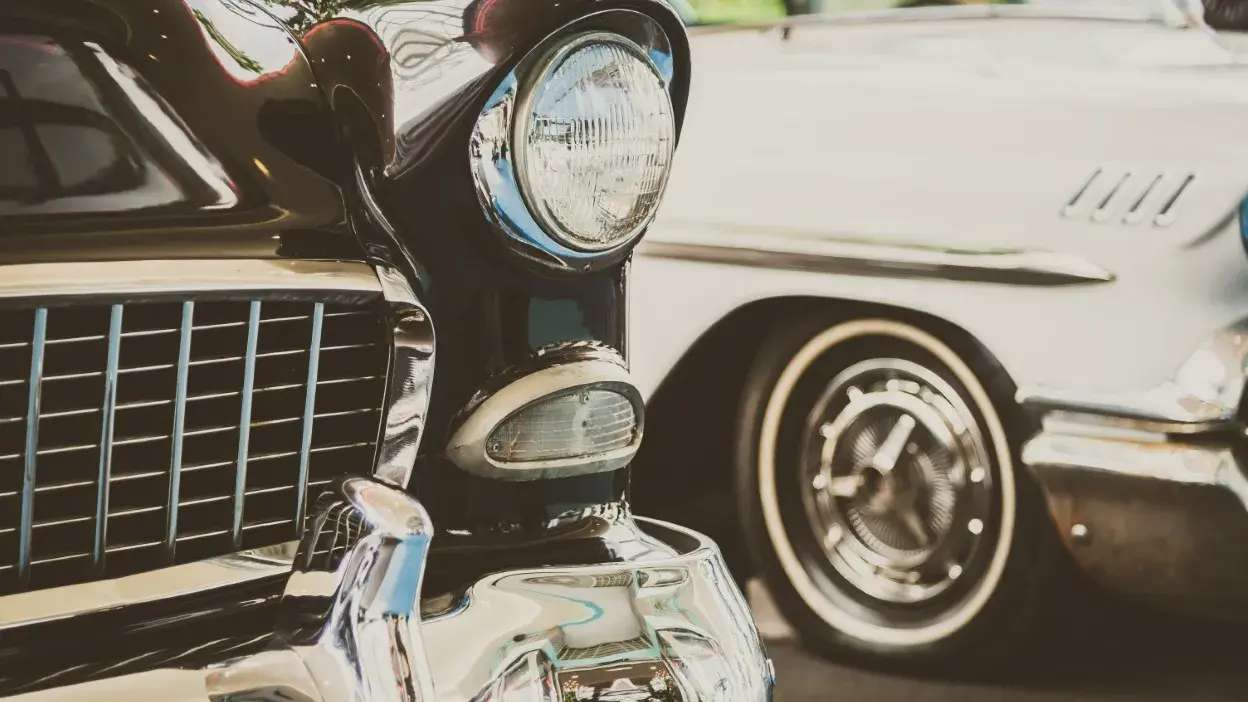 Detalhe dos faróis e grelha de dois carros clássicos estacionados lado a lado.