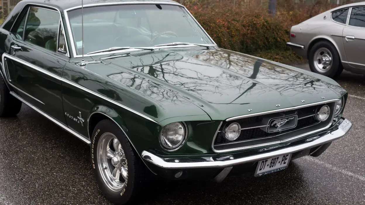 Carro clássico Ford Mustang verde escuro estacionado, visto de frente e lado esquerdo.