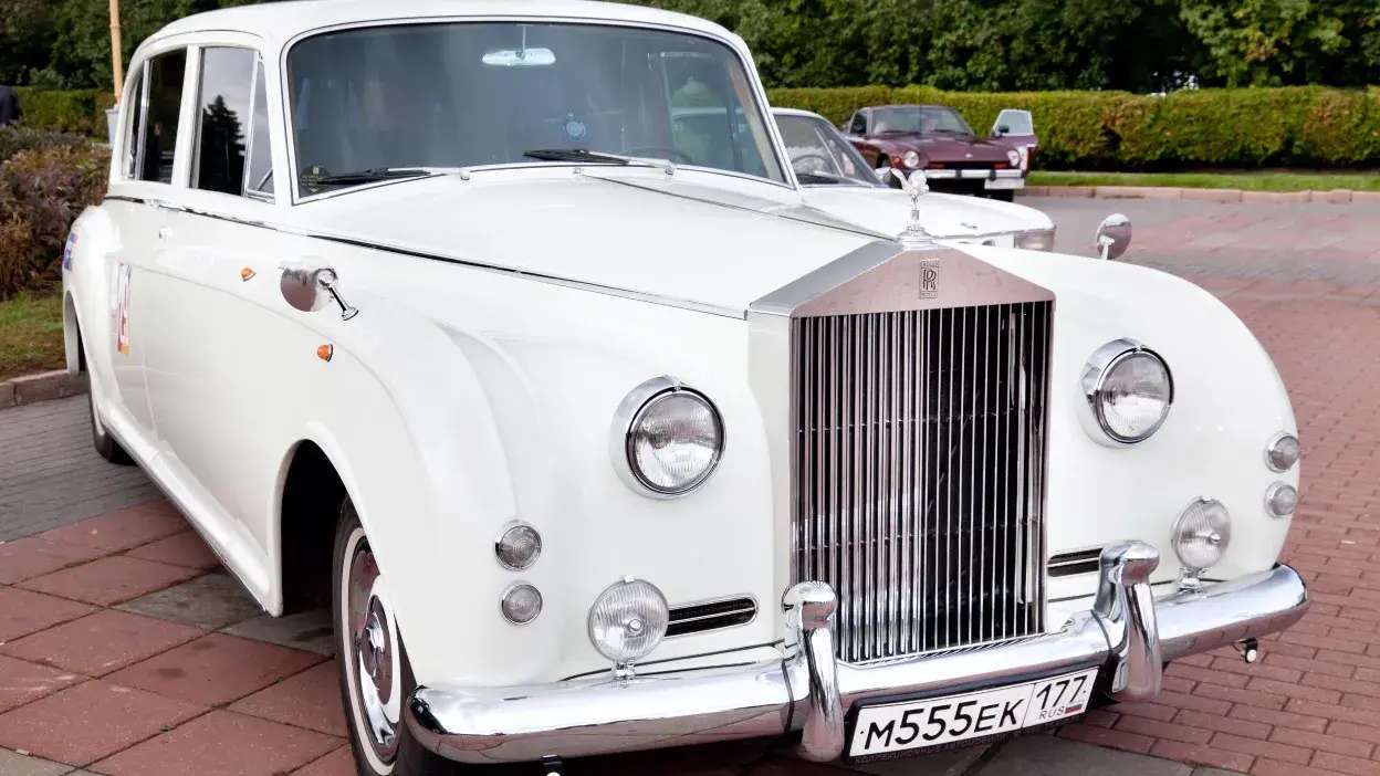 Carro clássico branco Rolls-Royce estacionado numa rua com outros carros ao fundo