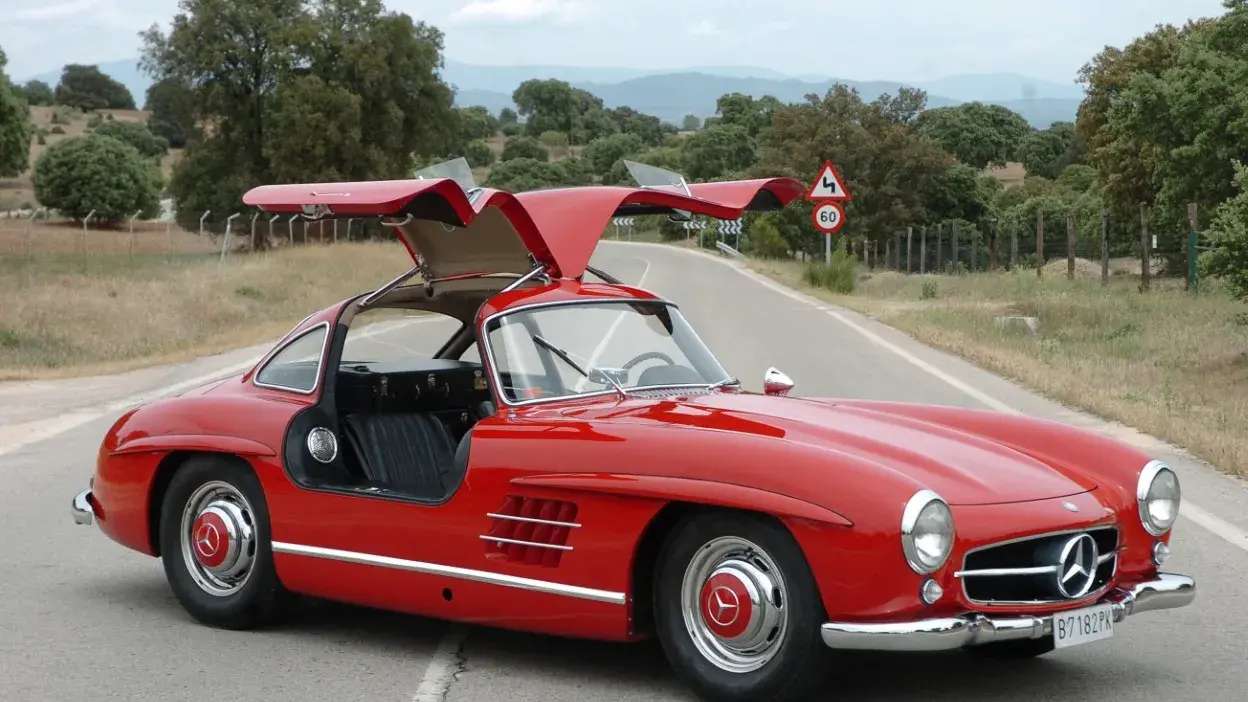 Carro desportivo clássico vermelho com portas asa de gaivota aberto numa estrada rural