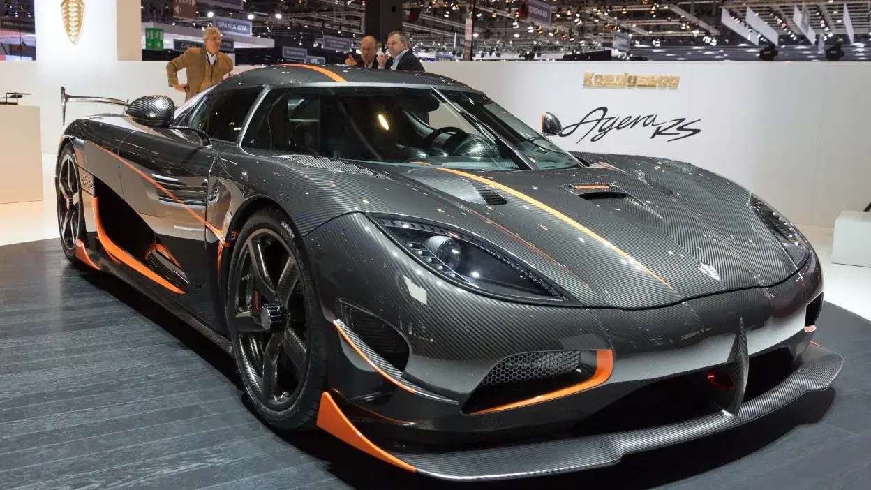 Carro desportivo Koenigsegg Agera RS em exposição, com acabamento em fibra de carbono e detalhes laranja.