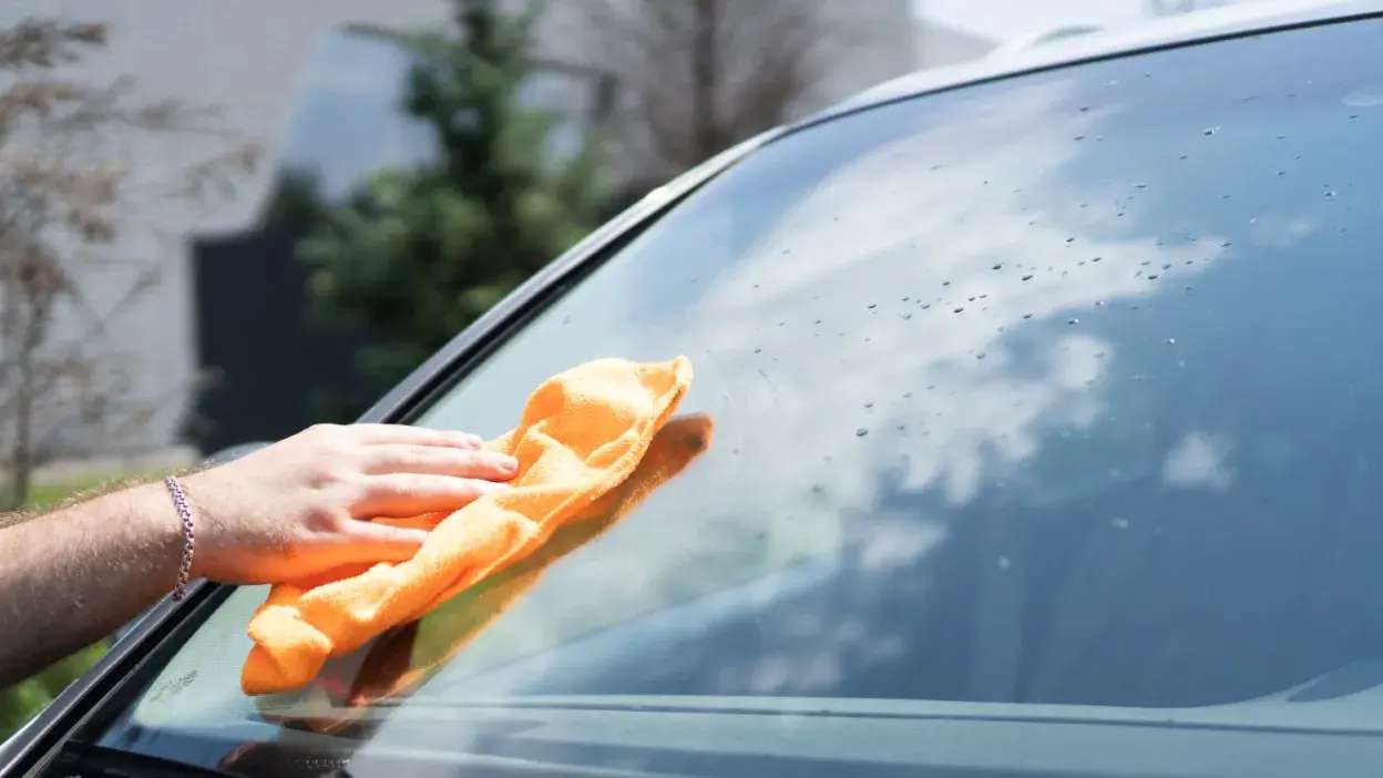 Mão a limpar vidro de carro com pano laranja
