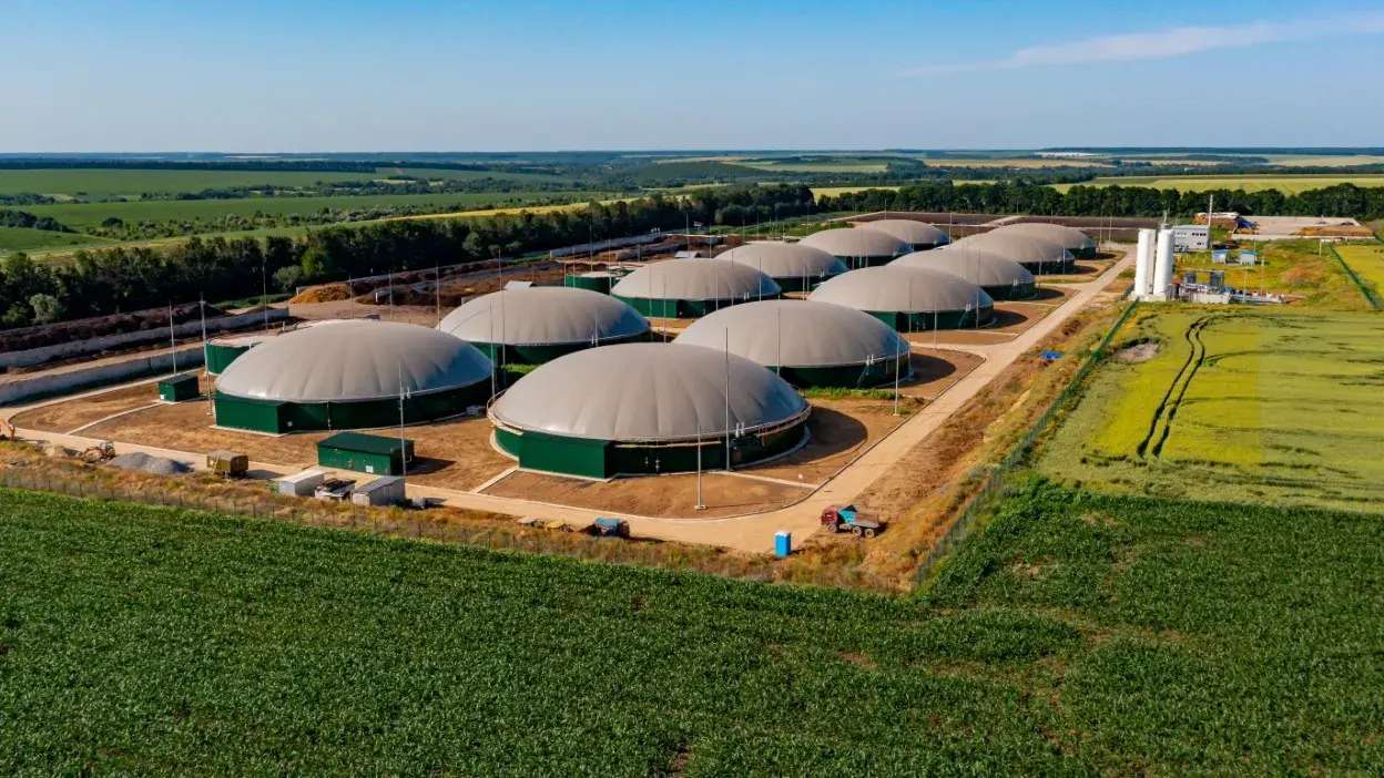 Vista aérea de central de biocombustíveis com tanques de armazenamento rodeada por campos agrícolas.