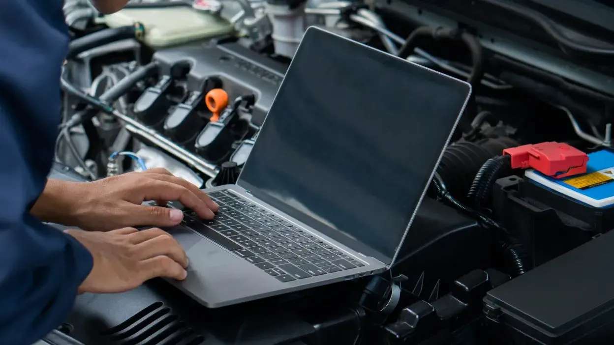 Pessoa a usar portátil para diagnóstico no motor de um carro aberto