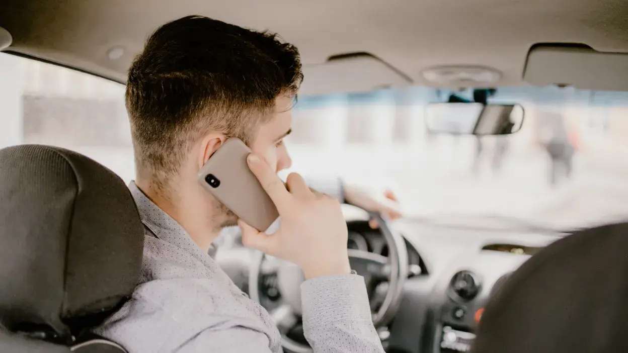 Homem a conduzir um carro enquanto fala ao telemóvel com a mão direita.
