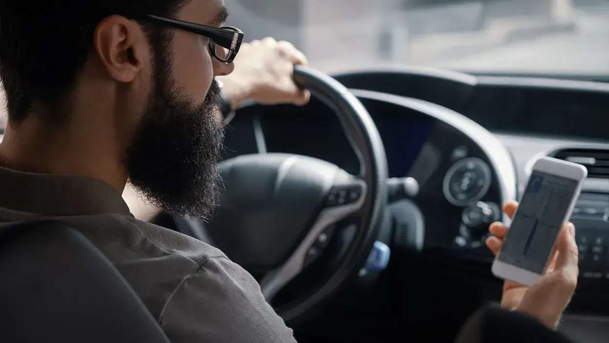 Homem a conduzir e a olhar para o telemóvel dentro de um carro